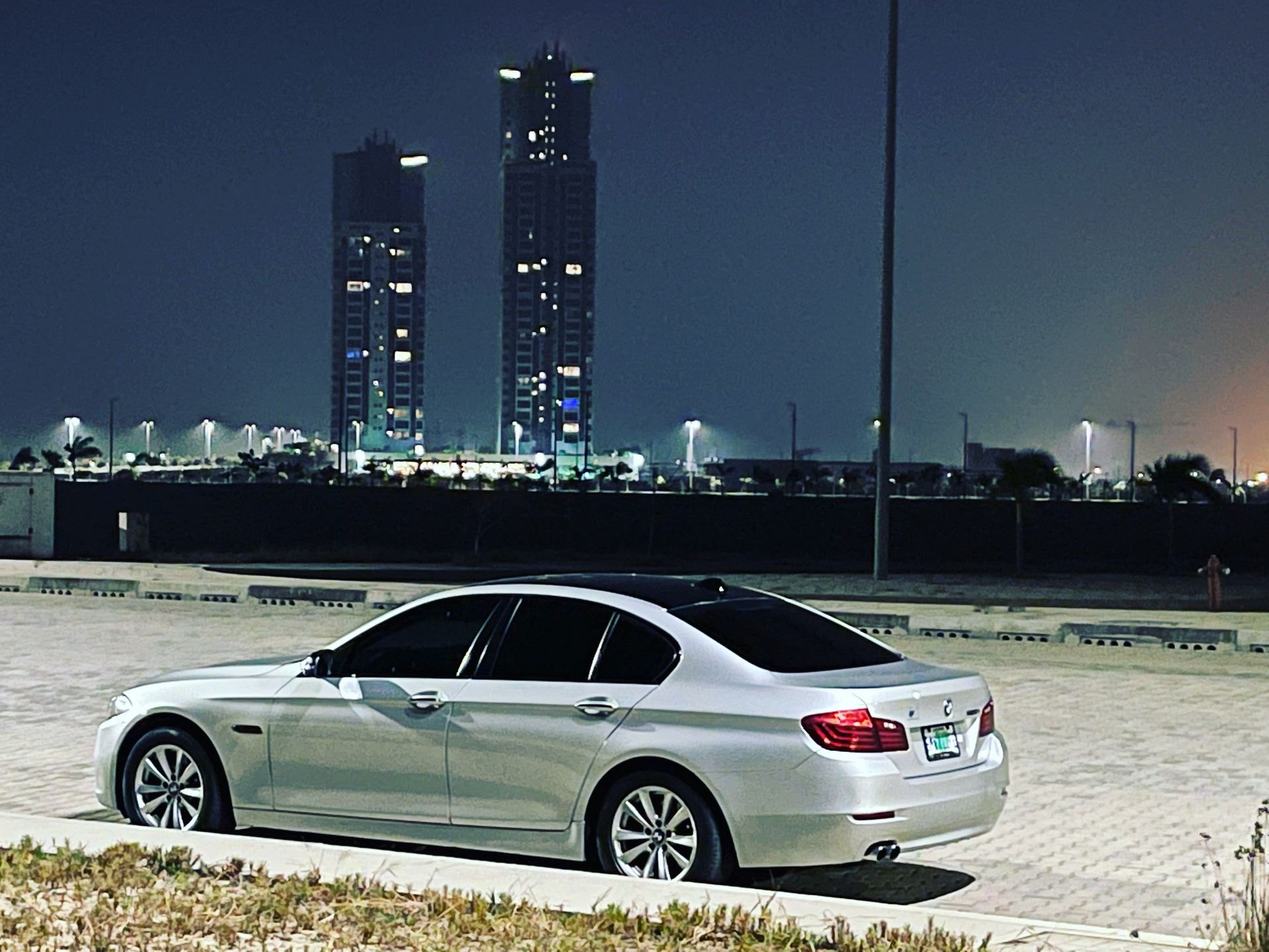 A BMW 5 Series parked at night against the Eko Atlantic skyline in Lagos
